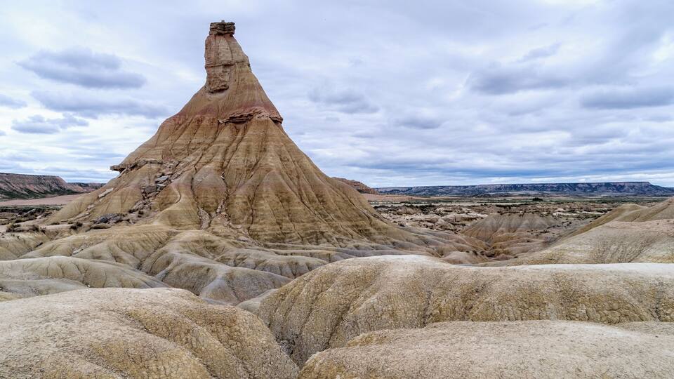 A unique rock formation with a tall, narrow peak surrounded by rugged, layered terrain.