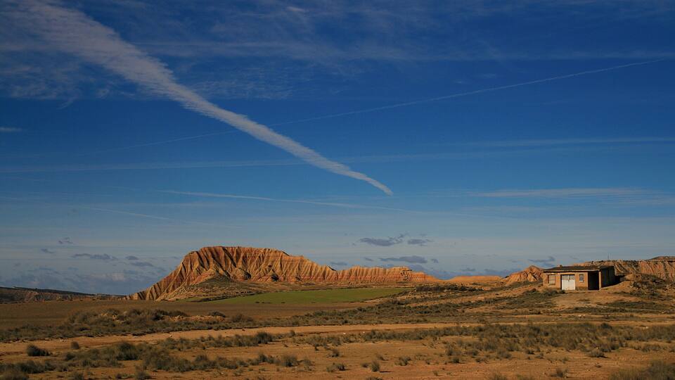 A desert landscape with a prominent rock formation and a small building.