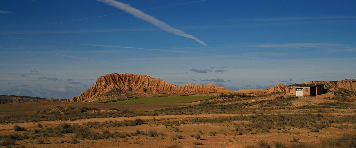A desert landscape with a prominent rock formation and a small building.