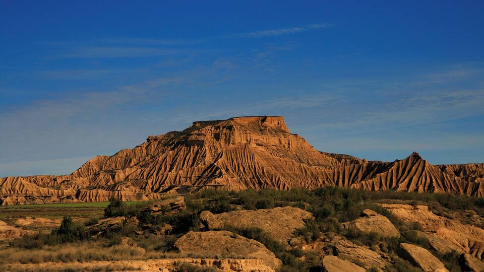 A rugged mountain with a flat top, surrounded by rocky terrain and sparse vegetation.