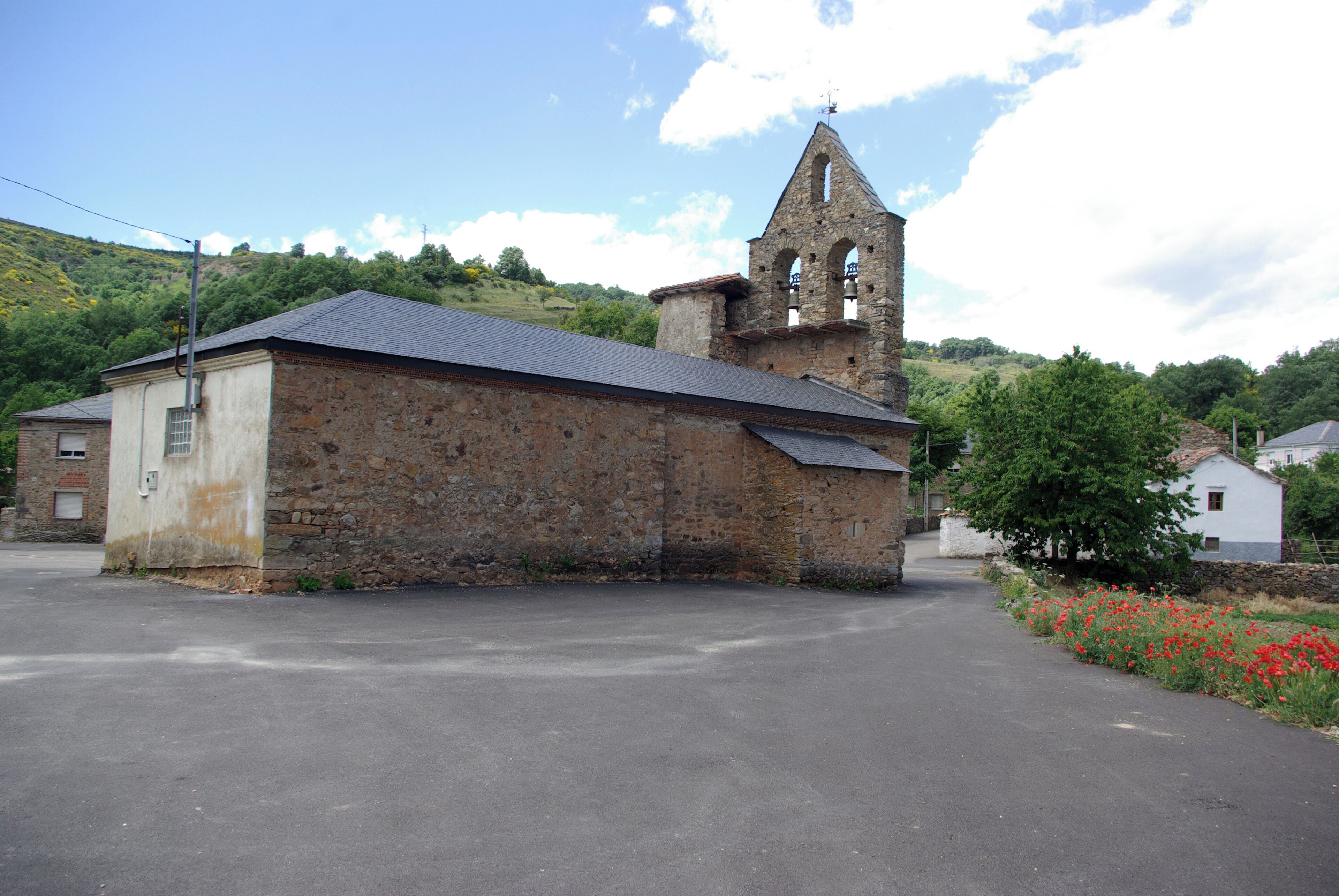 A stone church with a bell tower and a paved road in front.