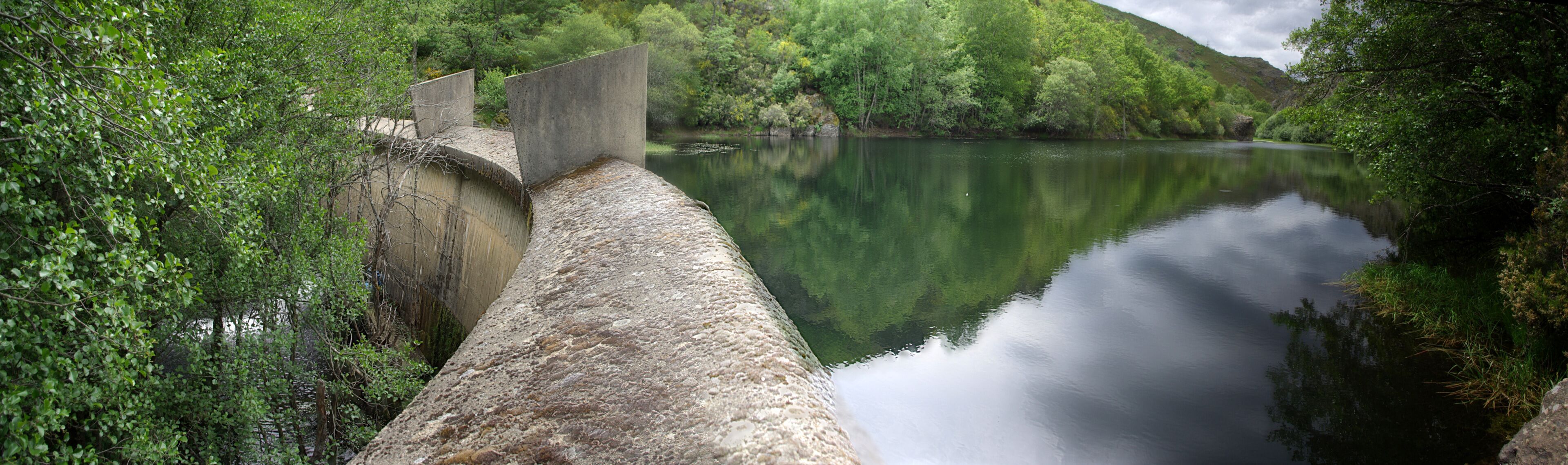 A concrete dam with a river in a forested valley.