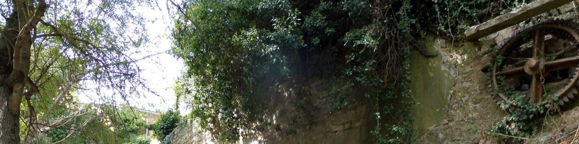 An ancient stone wall with a water wheel and stone benches.