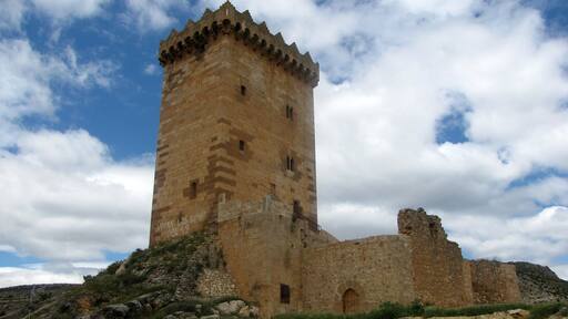 Una torre de piedra histórica con almenas, rodeada de terreno rocoso y vegetación escasa.