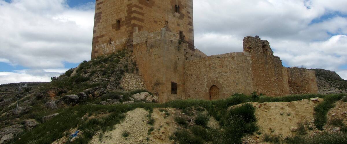 A historic stone tower with battlements, surrounded by rocky terrain and sparse vegetation.