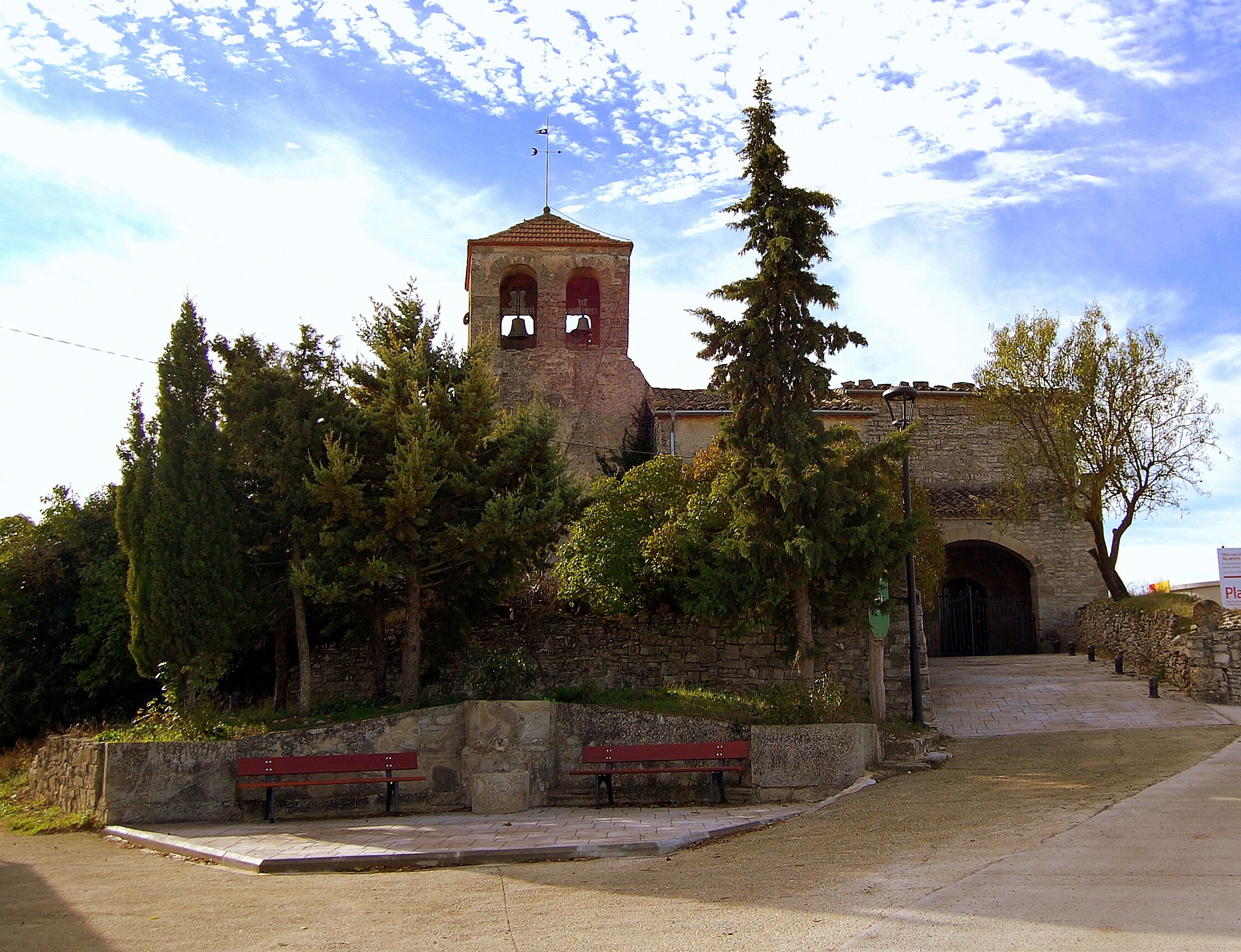 A church with a bell tower, surrounded by trees and benches.