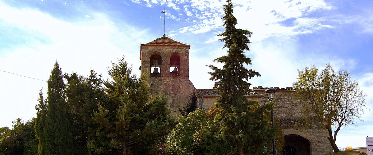 A church with a bell tower, surrounded by trees and benches.