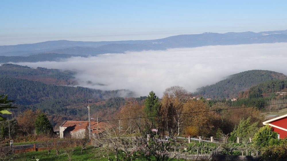 A mountainous landscape with a valley shrouded in mist, a red-roofed building, and a distant hill with a white structure.