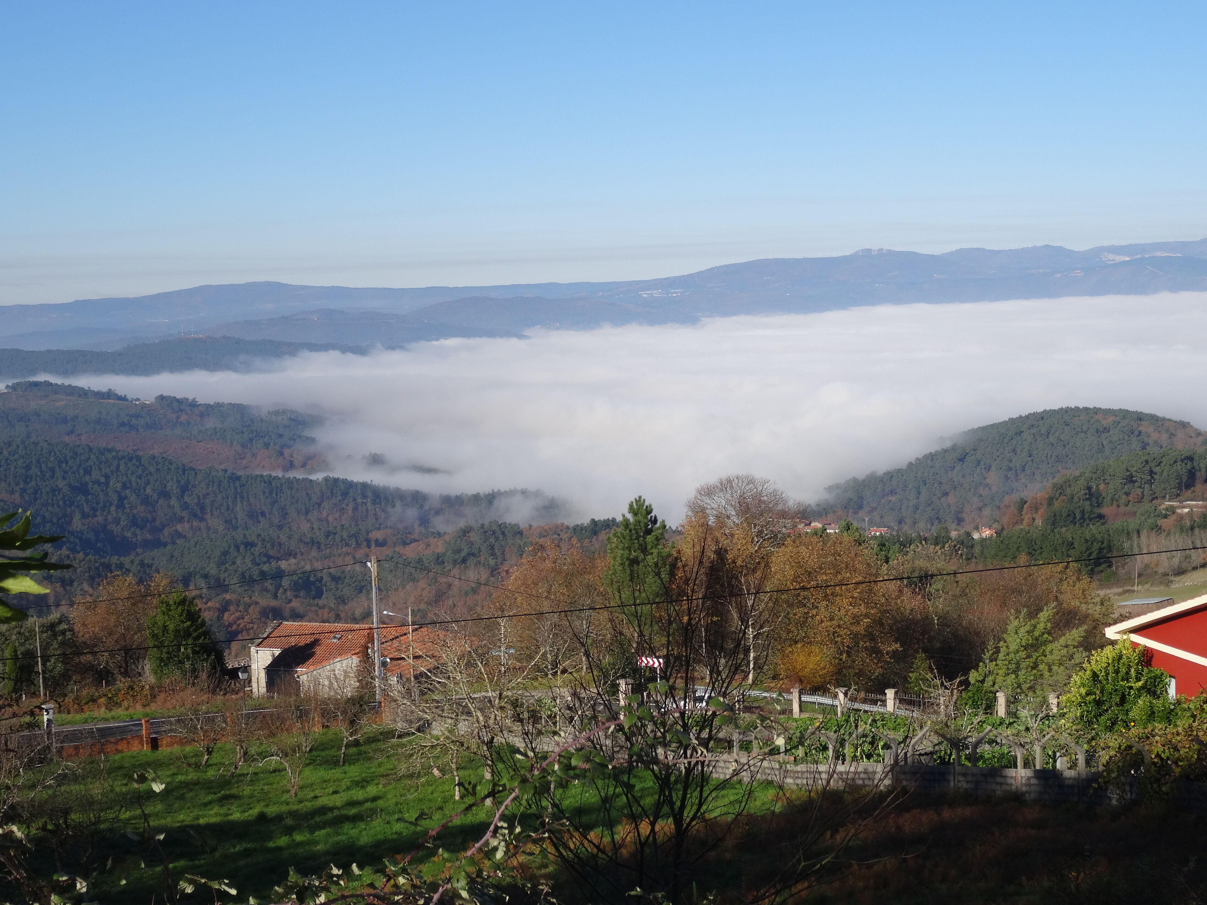 A mountainous landscape with a valley shrouded in mist, a red-roofed building, and a distant hill with a white structure.