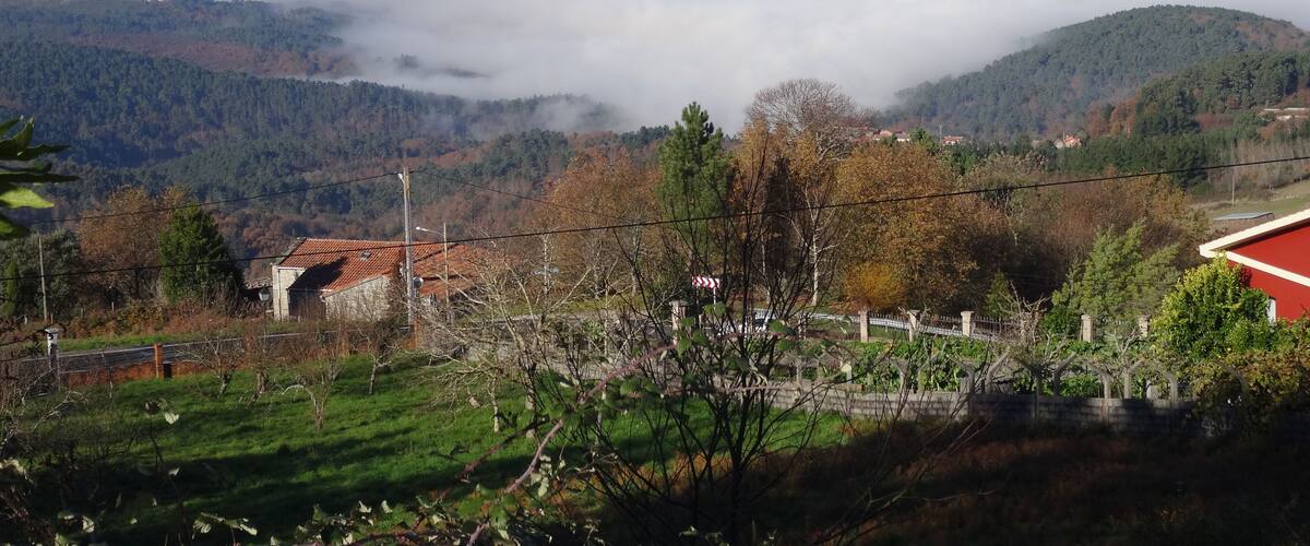 A mountainous landscape with a valley shrouded in mist, a red-roofed building, and a distant hill with a white structure.
