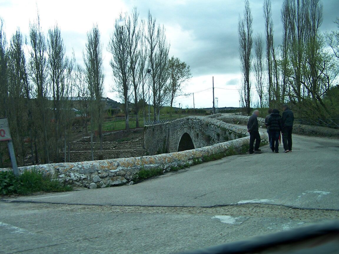 A rural road with a stone bridge, leafless trees, and a stone wall.