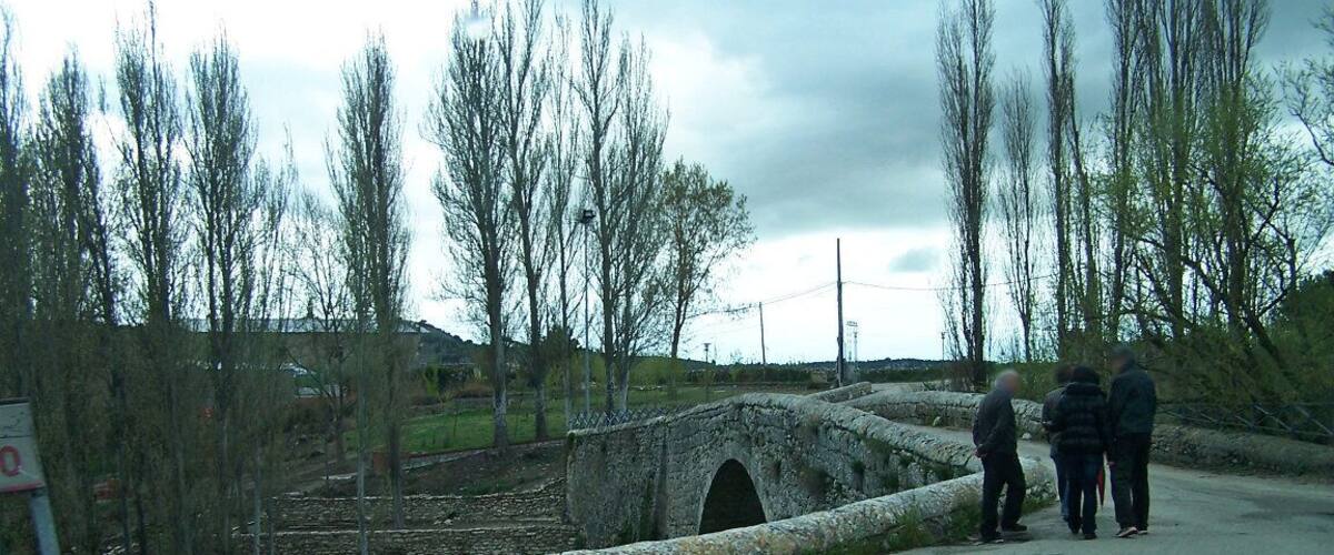 A rural road with a stone bridge, leafless trees, and a stone wall.