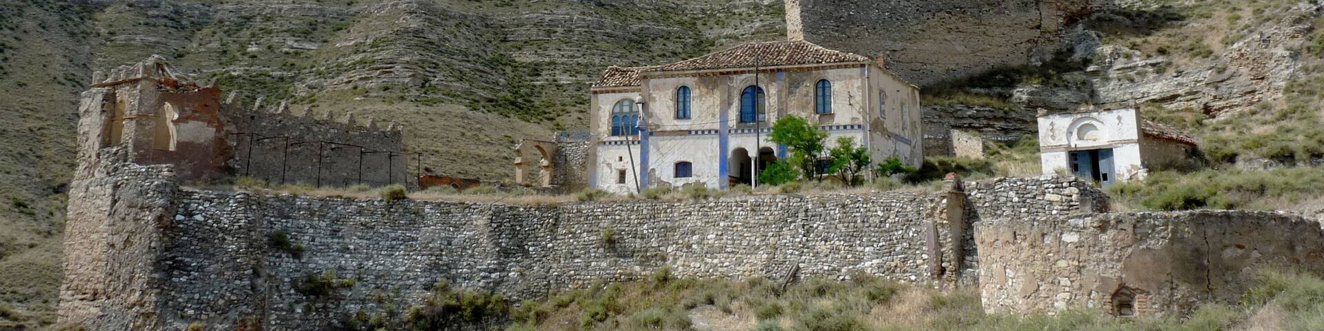 A historical building with blue doors and windows, surrounded by stone walls and ruins on a hillside.