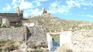 An ancient stone structure with ruins and a small building with arched windows.