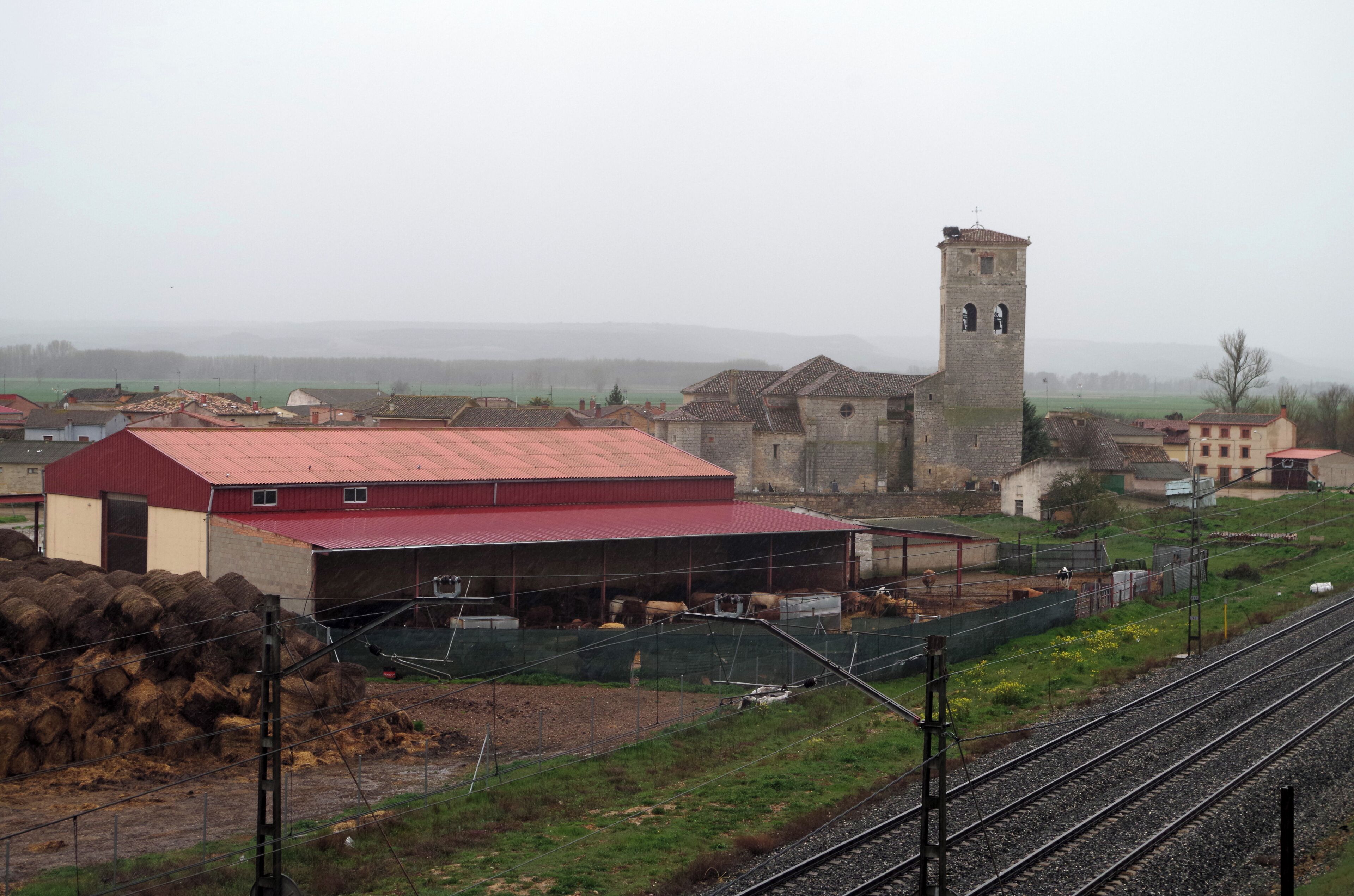 A rural landscape with a stone tower, a red-roofed barn, and railway tracks.