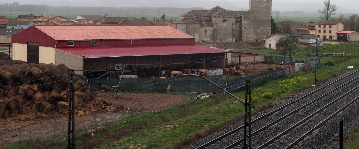 A rural landscape with a stone tower, a red-roofed barn, and railway tracks.