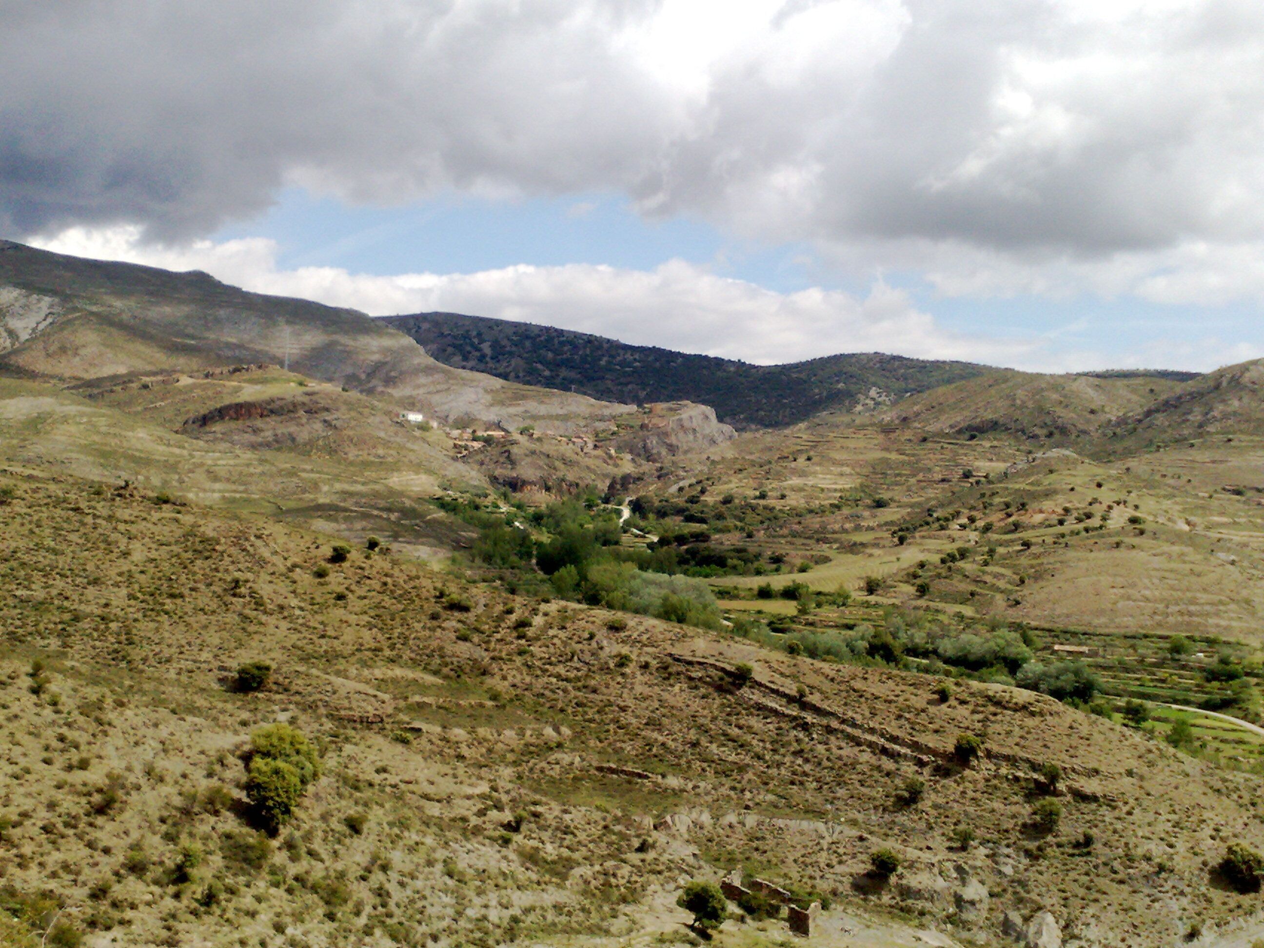 A rugged mountainous landscape with a winding road and scattered vegetation.