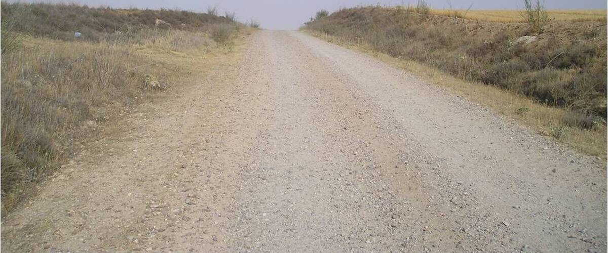 A gravel road in a dry, open landscape with sparse vegetation.