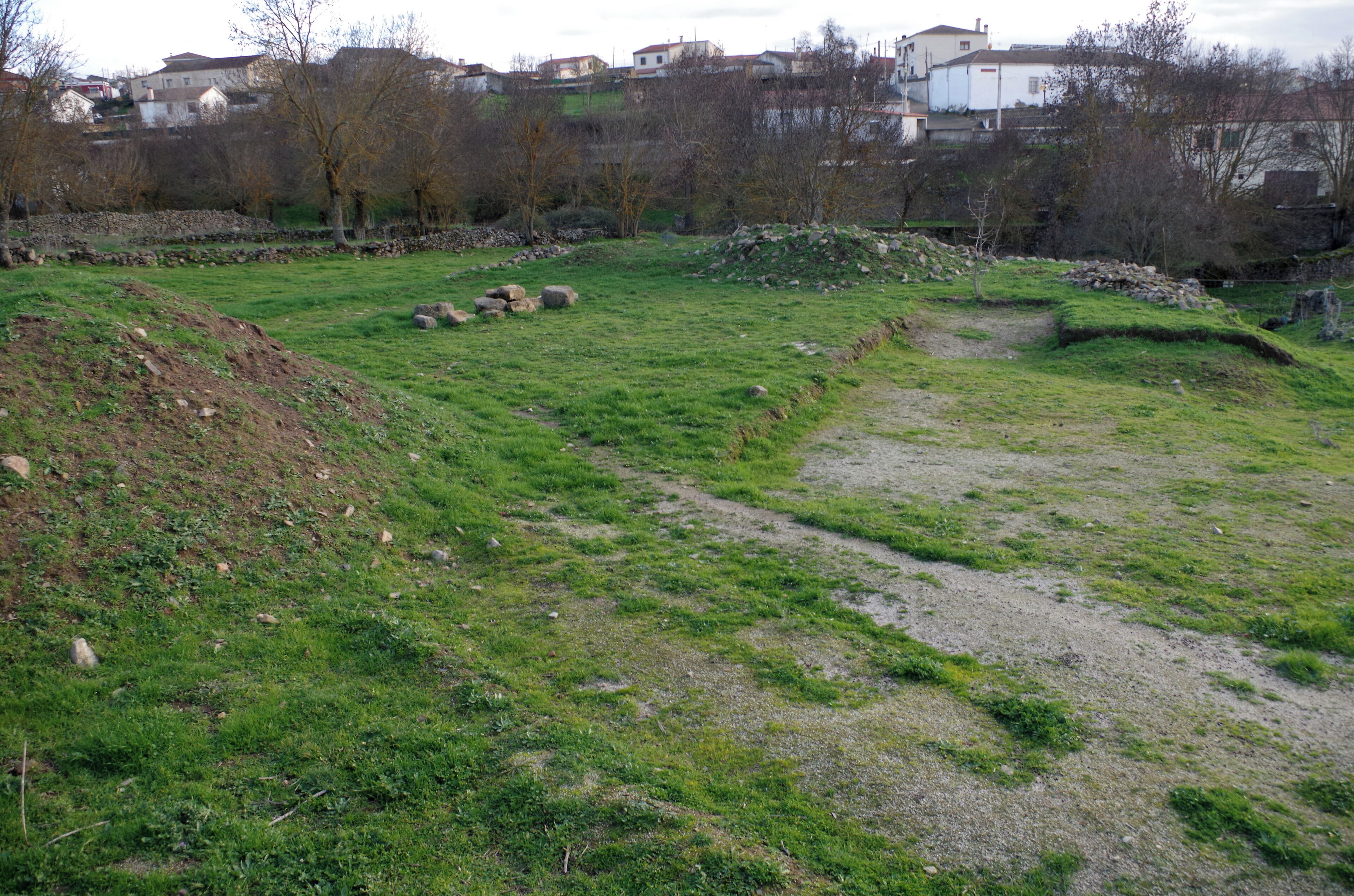 A grassy field with a dirt path, scattered rocks, and a stone wall.