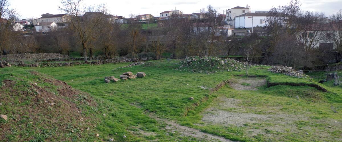 A grassy field with a dirt path, scattered rocks, and a stone wall.