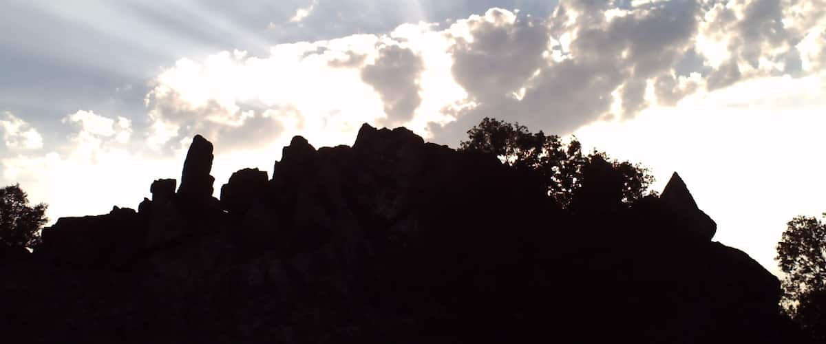 A silhouette of a rocky outcrop with rays of sunlight piercing through the clouds.