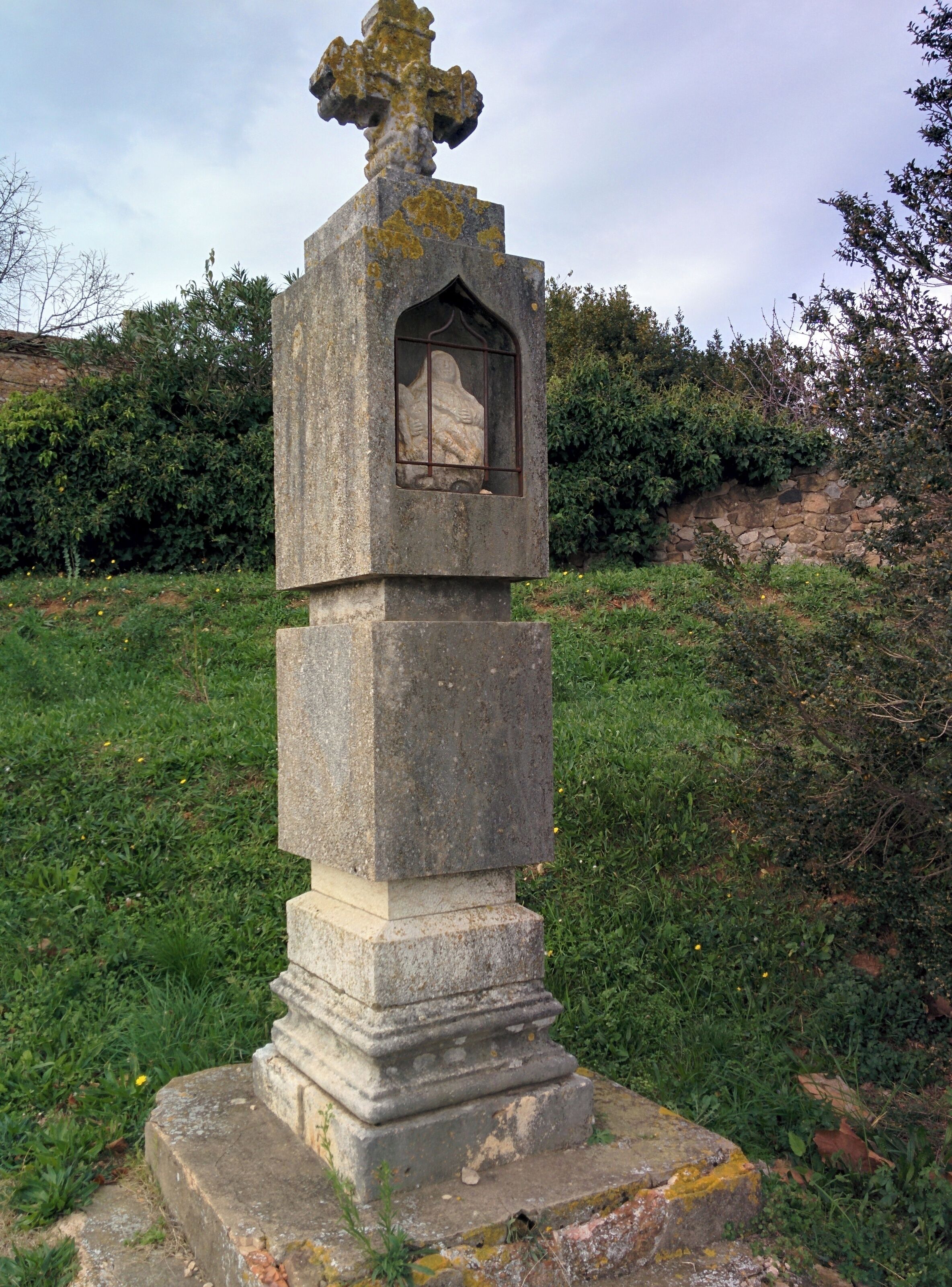 A stone monument with a cross on top and a carved figure inside a window.