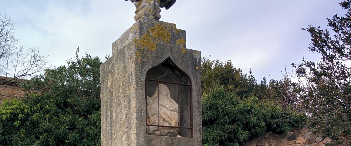 A stone monument with a cross on top and a carved figure inside a window.