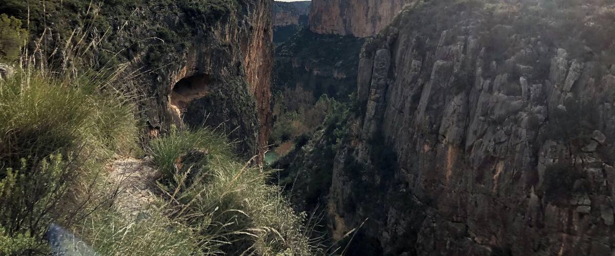 A canyon with steep cliffs and a small cave entrance.