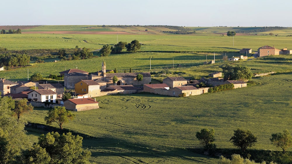 A rural village with stone buildings, terraced fields, and rolling hills in the background.
