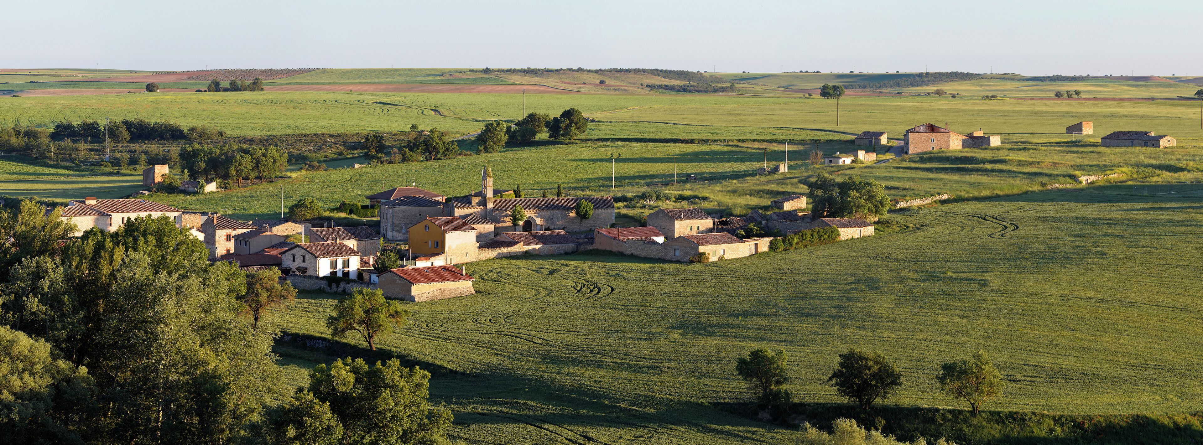 A rural village with stone buildings, terraced fields, and rolling hills in the background.