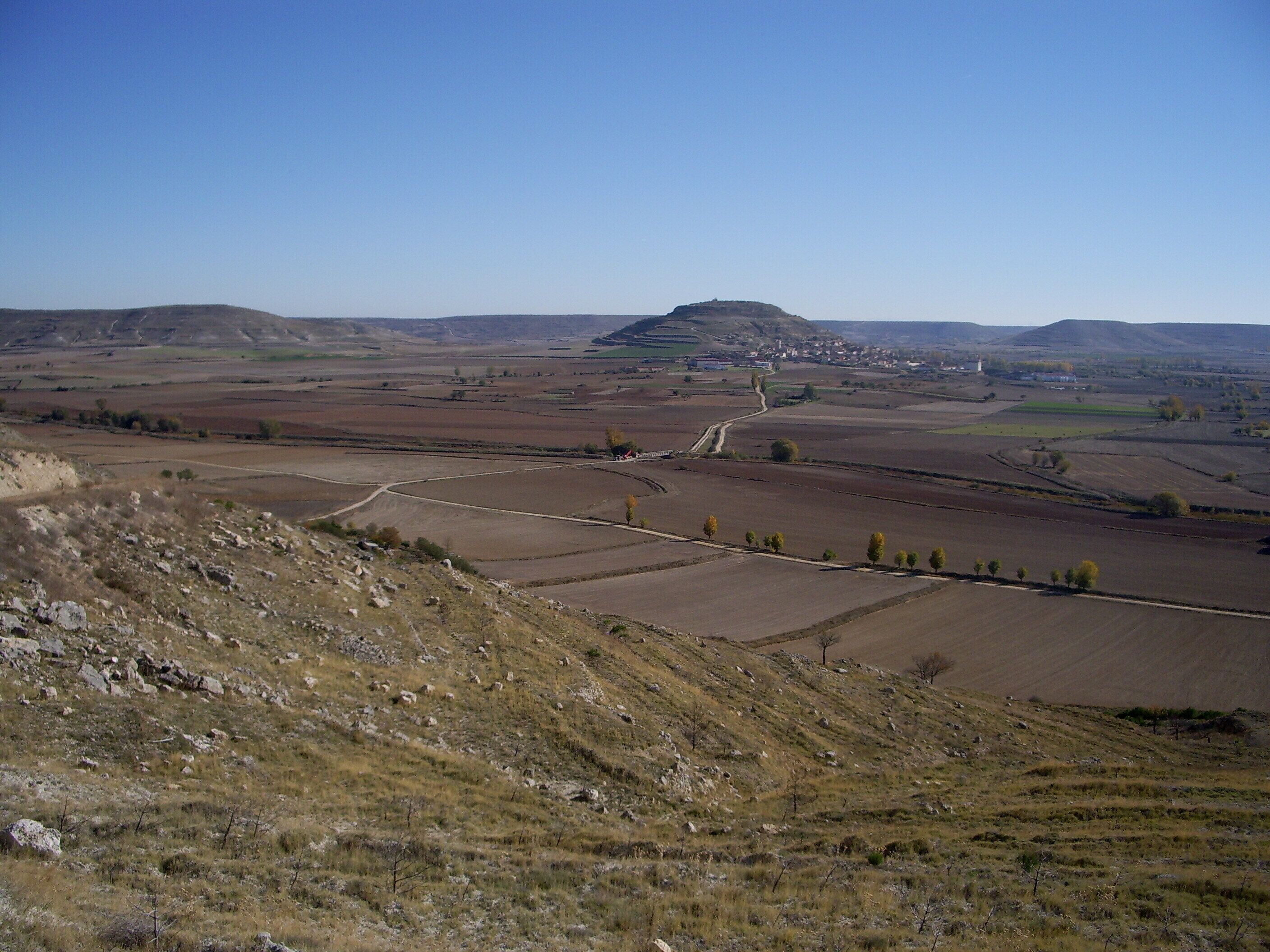 A rural landscape with rolling hills, fields, and a distant village.