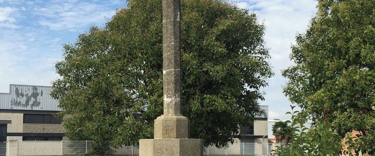 A stone cross monument with a cross on top, surrounded by grass and trees.