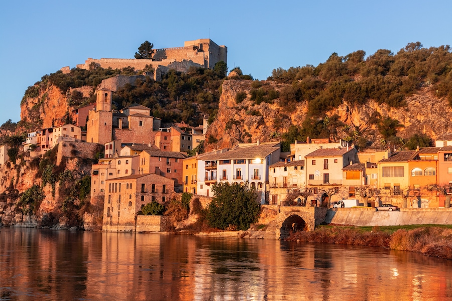 A coastal town with historic stone buildings, a river, and a castle on a hill.