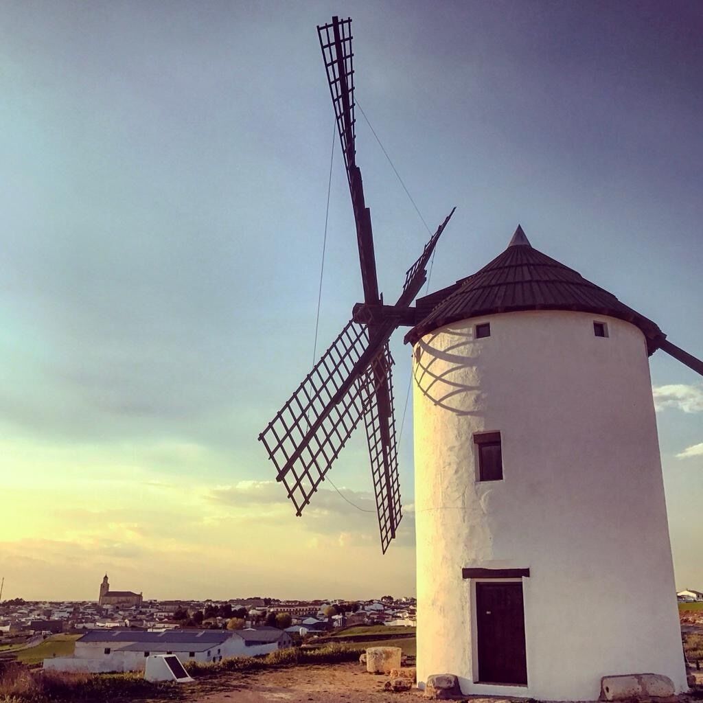 A traditional windmill with a white body and dark roof, set against a clear sky.