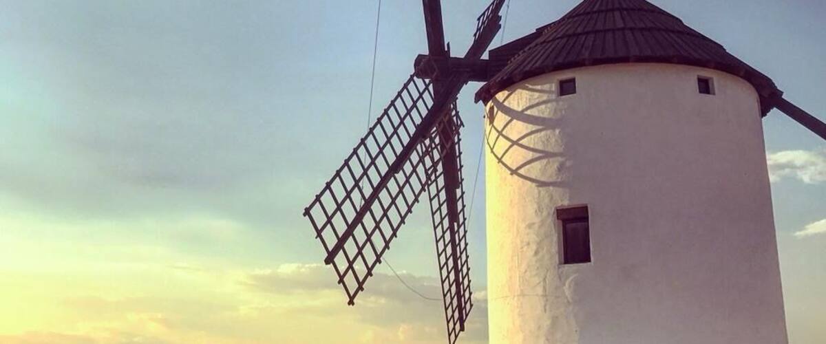 A traditional windmill with a white body and dark roof, set against a clear sky.