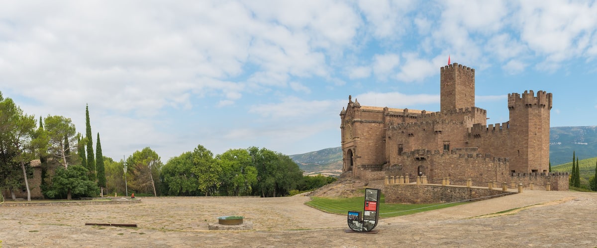 A historic castle with a prominent tower, surrounded by a stone courtyard and lush greenery.