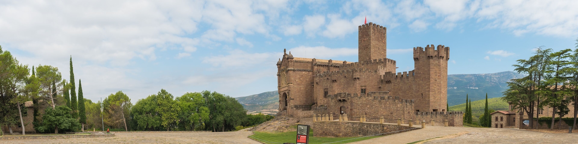 A historic castle with a prominent tower, surrounded by a stone courtyard and lush greenery.