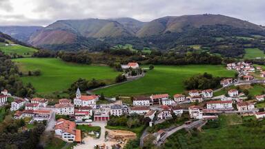 A village nestled in a valley with green fields, a church, and houses with red roofs.