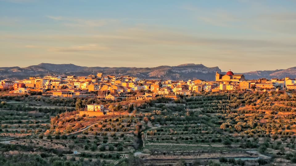A town with a prominent church with a red dome, surrounded by hills and dry vegetation.