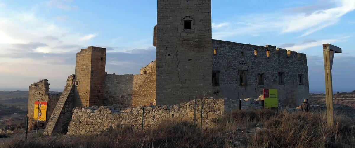 A medieval stone tower with a rectangular base and a smaller tower on top, surrounded by dry grass and a clear sky.