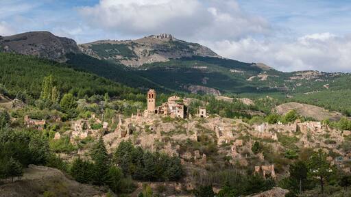 Un paisaje montañoso con ruinas y bosques densos.
