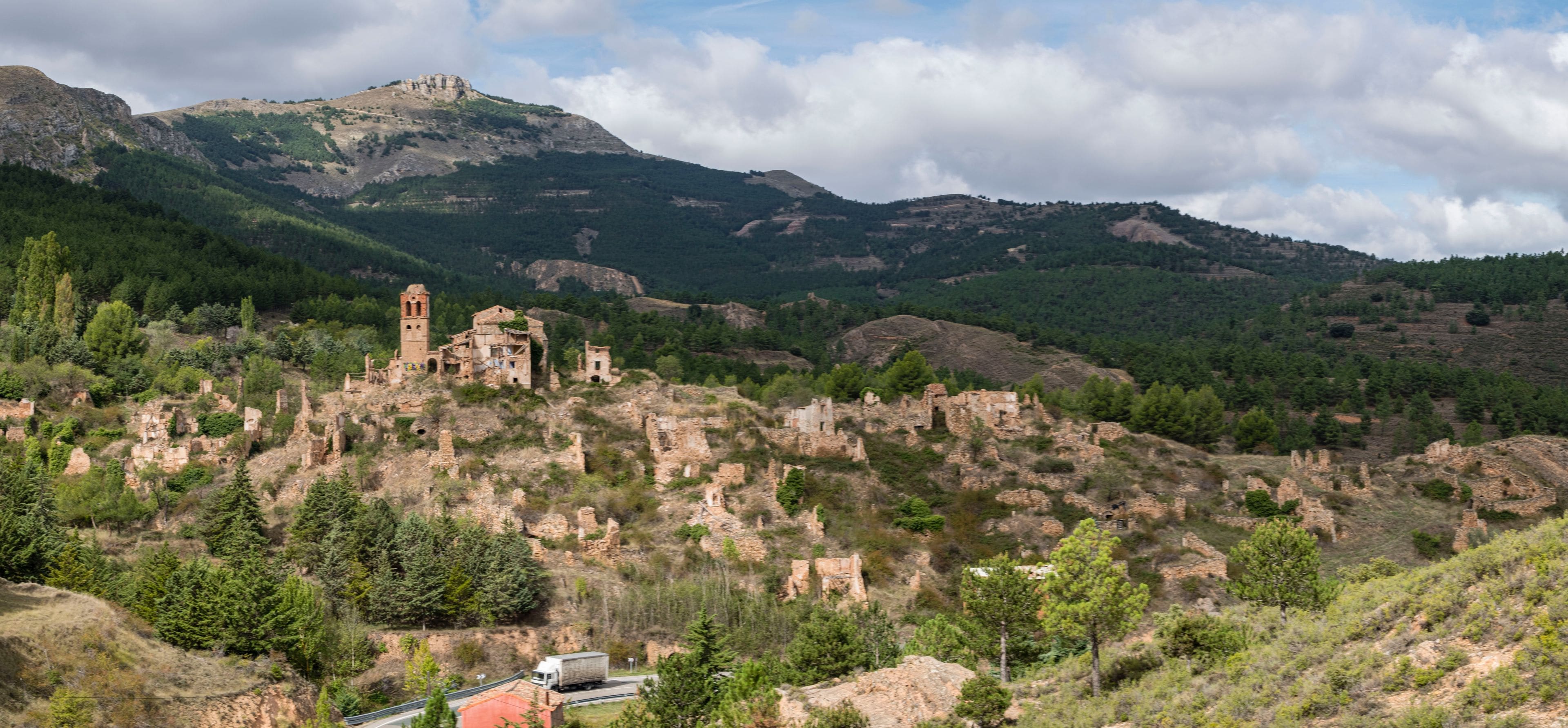 Paisatge montanyós amb ruïnes i una torre.