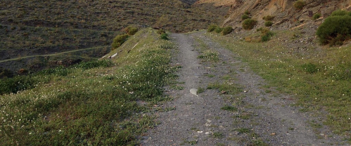 A narrow mountain path flanked by rocky hills and sparse vegetation.