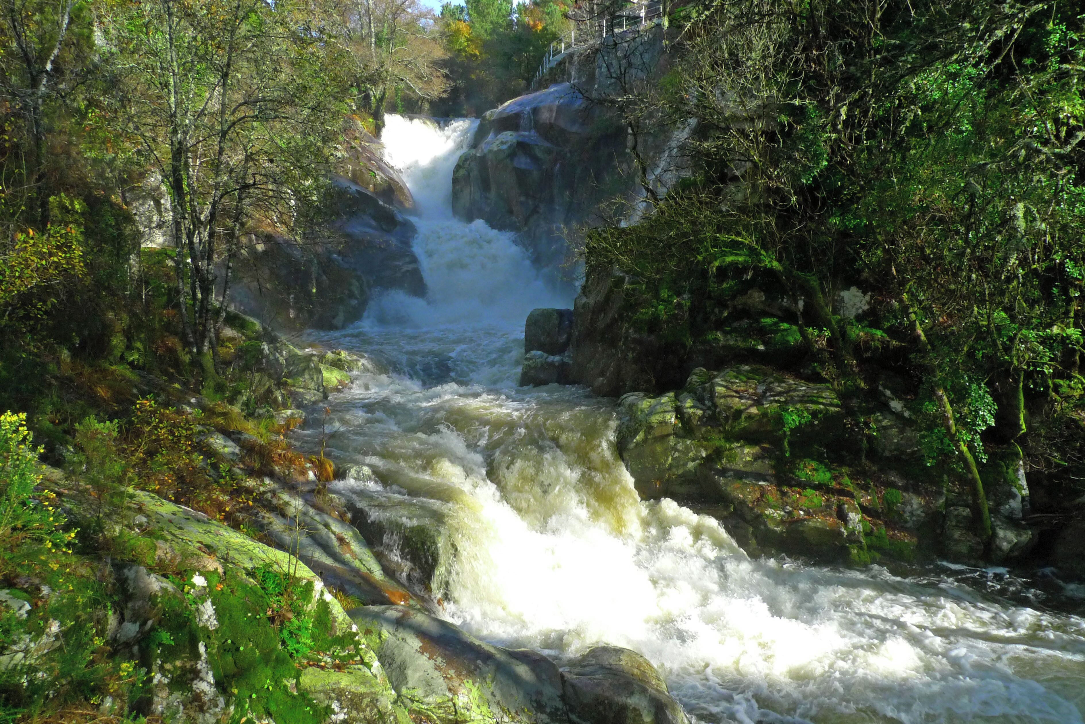 A waterfall surrounded by lush greenery and rocky terrain.