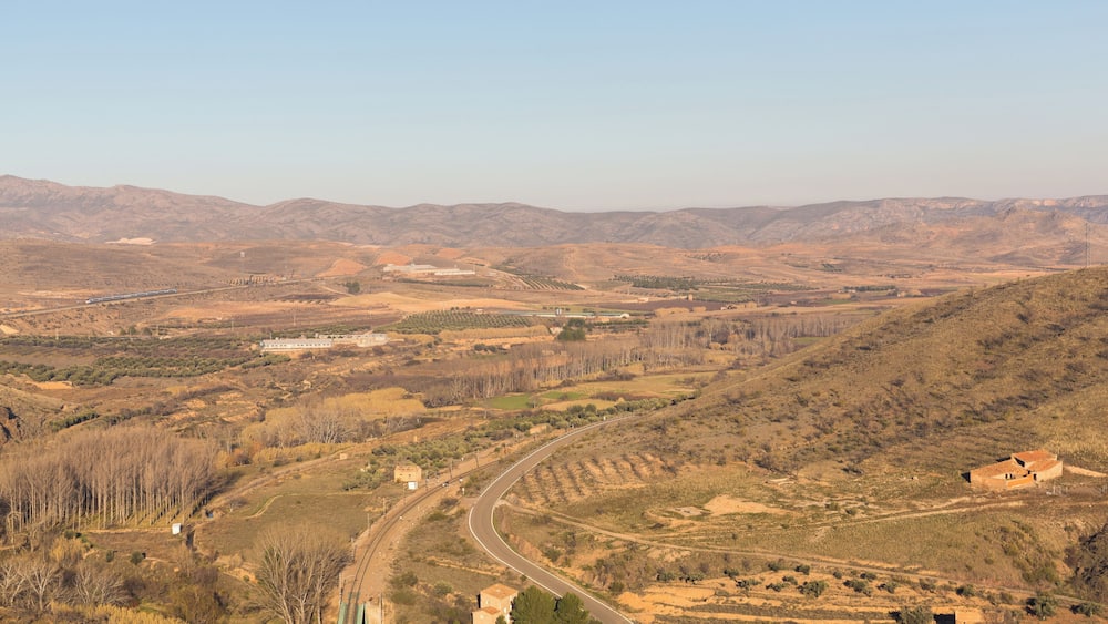 Eine kurvenreiche Straße durch eine hügelige Landschaft mit spärlicher Vegetation und fernen Bergen.