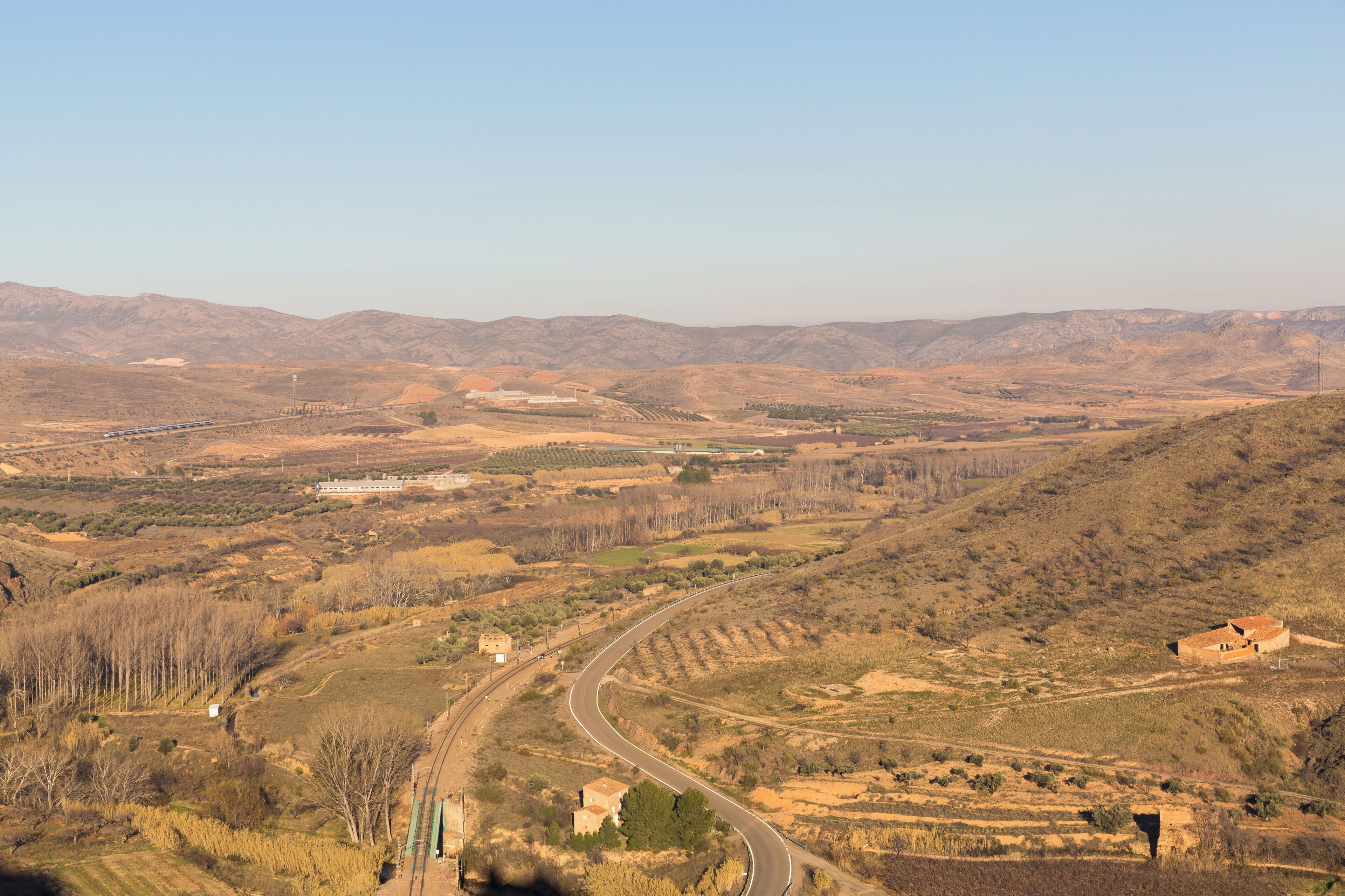 A winding road through a hilly landscape with sparse vegetation and distant mountains.