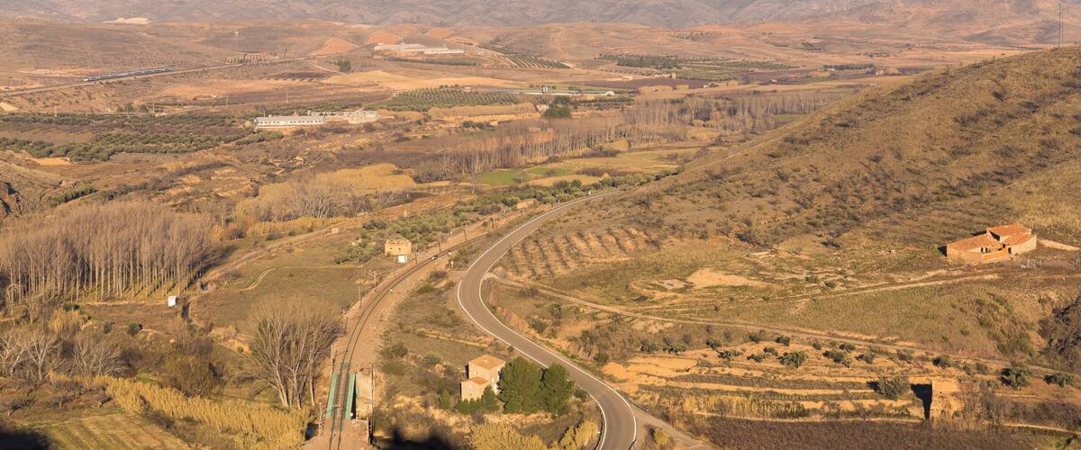A winding road through a hilly landscape with sparse vegetation and distant mountains.