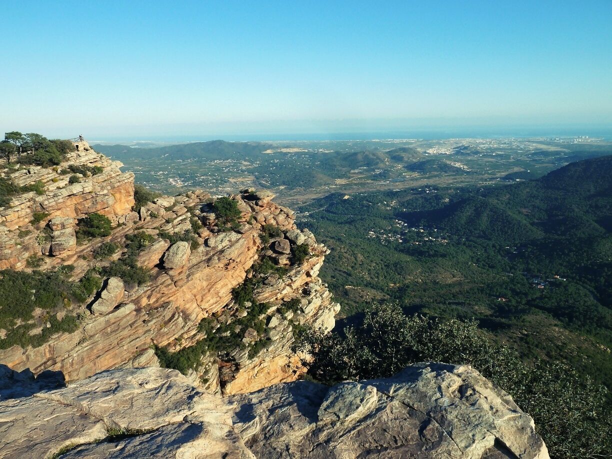 A rocky cliff overlooking a valley with scattered buildings and greenery.