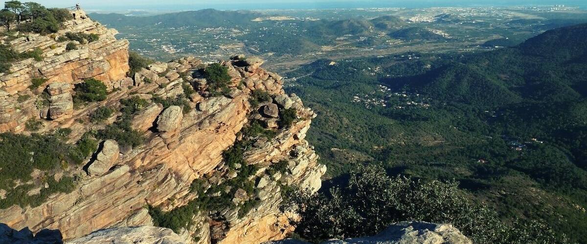 A rocky cliff overlooking a valley with scattered buildings and greenery.