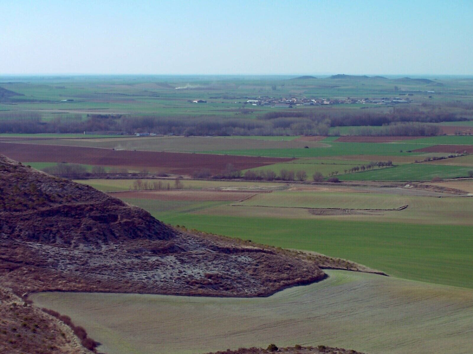 A rural landscape with rolling hills, fields, and a small village in the distance.
